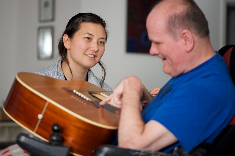 Disability worker watches man with a disability play guitar